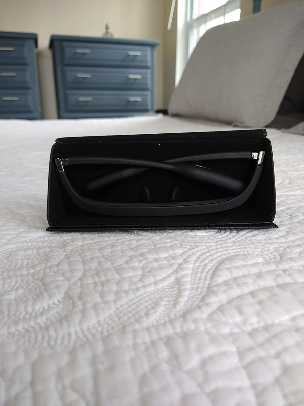 LUNO Vision glasses in their case on a bed in a bright bedroom — symbol of calm and daily recovery ritual.